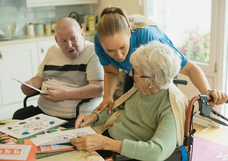 Caregiver helping two older adults with an activity at a kitchen table