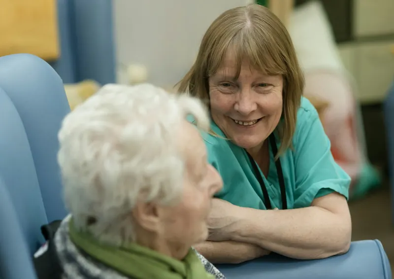 Caregiver in scrubs talking warmly with an older woman