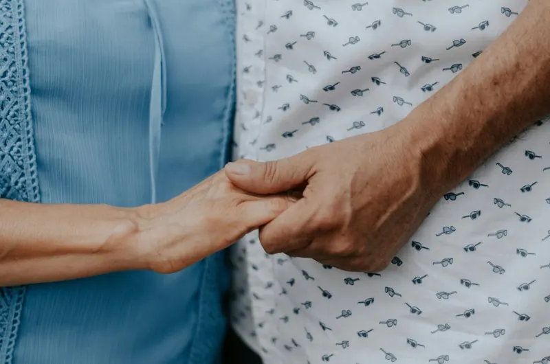 Two people holding hands at a bedside