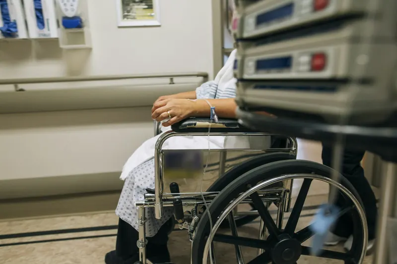 Patient in a hospital gown seated in a wheelchair in a hospital room