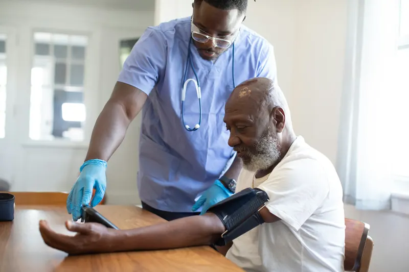 Illustrative stock photo: Nurse checking an older man's blood pressure at a table at home